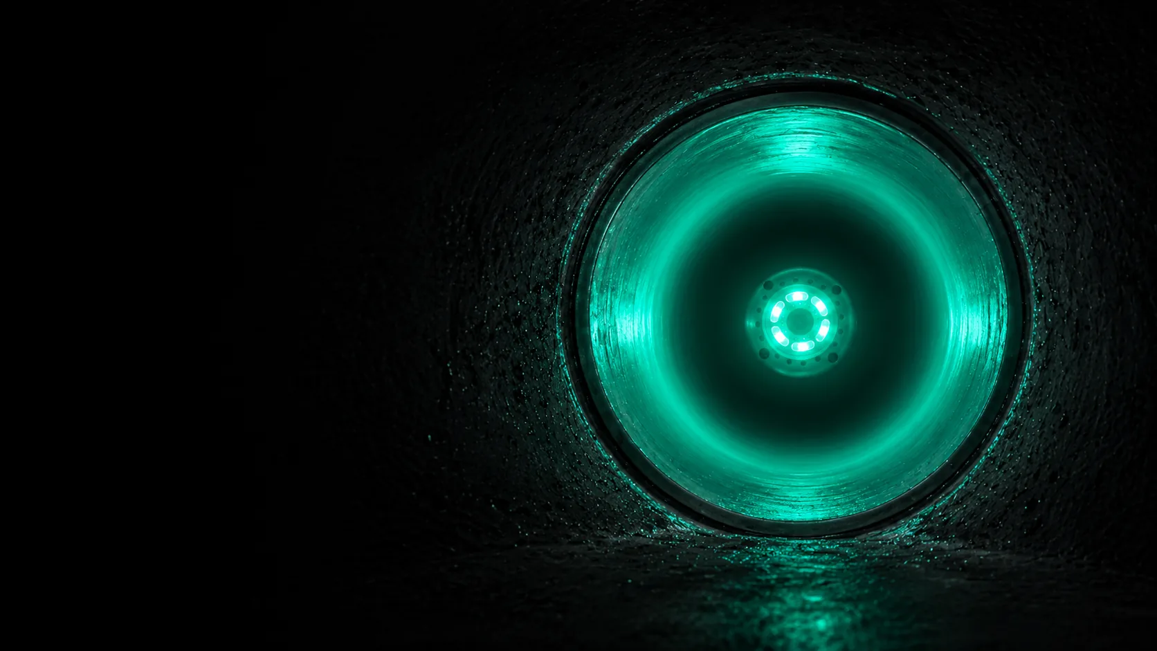 Interior view of a rehabilitated pipeline illuminated with a green curing light, showing smooth new pipe wall.